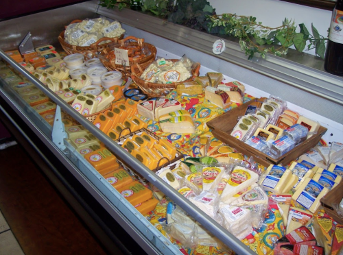 A display case filled with various types of cheese, including blocks, slices, and spreads, arranged attractively.