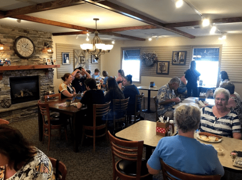 A busy restaurant interior with diners at tables, a stone fireplace, and wall decor, creating a cozy atmosphere.