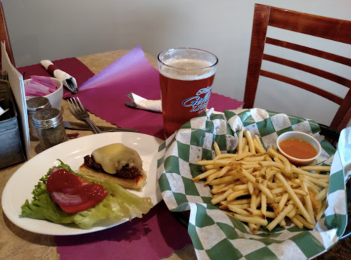 A plate with a cheeseburger, lettuce, and ketchup, alongside a basket of fries and a pint of beer on a table.