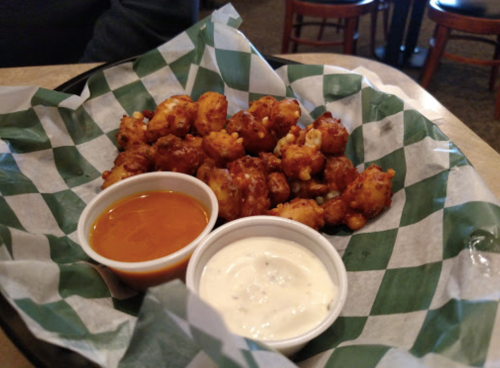 A plate of crispy, golden popcorn chicken served with two dipping sauces: one spicy and one creamy.