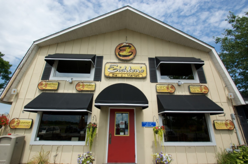 A charming market building with a red door, black awnings, and various signs for gifts, cheese, and nuts.