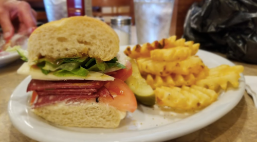 A close-up of a sandwich with layers of meat, cheese, lettuce, and tomato, served with waffle fries on the side.