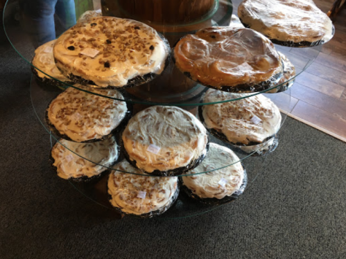 A display of various pies on a glass stand, covered with plastic wrap, showcasing different flavors and toppings.