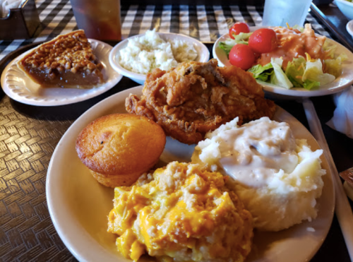 A plate of fried chicken, cornbread, mashed potatoes, macaroni and cheese, and a side salad with cherry tomatoes.
