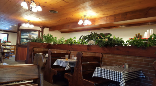 Cozy restaurant interior with wooden decor, checkered tablecloths, and greenery along the walls.