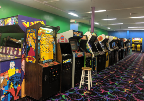 A row of vintage arcade machines in a colorful game room with a patterned carpet.