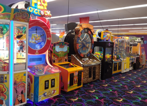 A colorful arcade with various games, including a spinning wheel and claw machines, on a vibrant carpet.