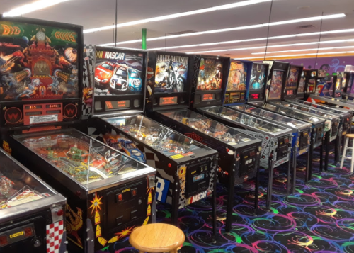 A row of colorful pinball machines in a vibrant arcade, featuring various themes and designs.