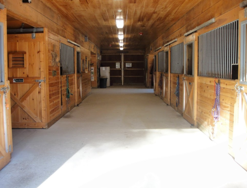 Interior of a wooden horse stable with empty stalls and a well-lit aisle.