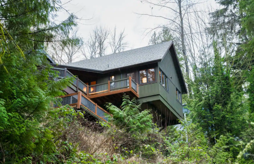 A modern green house perched on a hillside, surrounded by trees and greenery.