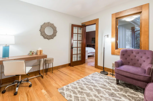 Cozy room featuring a desk, purple chair, mirror, and a doorway leading to another space with wooden accents.