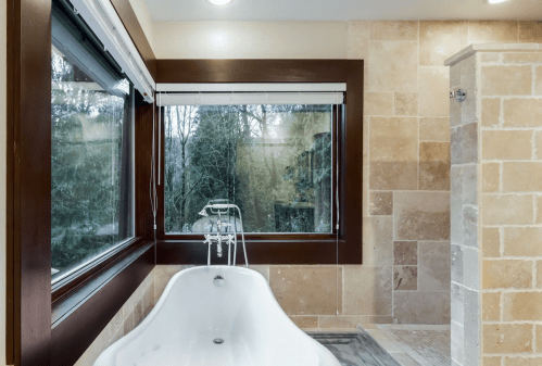 A modern bathroom featuring a freestanding tub, large windows, and stone tile walls.