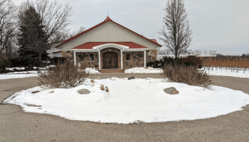 A stone building with a red roof surrounded by snow and bare trees, set in a rural landscape.