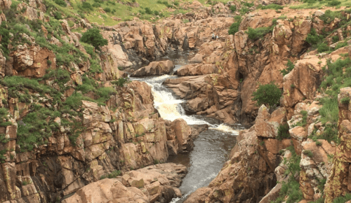 A scenic view of a rocky canyon with a flowing river and lush greenery on the surrounding hills.