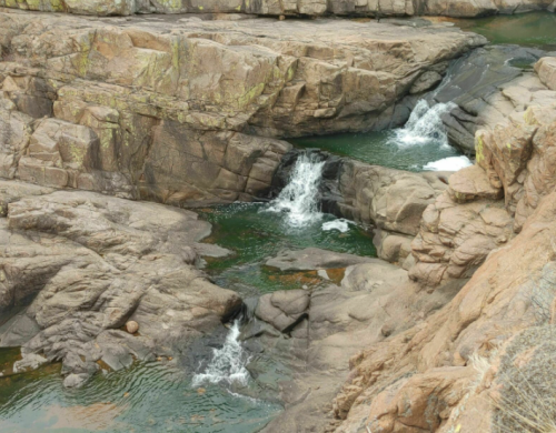 A rocky landscape with small waterfalls flowing into a greenish pool of water.