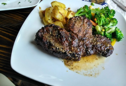 A plate featuring grilled steak, roasted potatoes, and a side of mixed vegetables including broccoli and carrots.