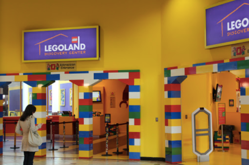 Entrance to Legoland Discovery Center, featuring colorful brick decor and a bright yellow interior.