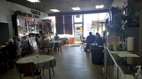 A cozy café interior with patrons seated at tables, vintage decor, and large windows letting in natural light.