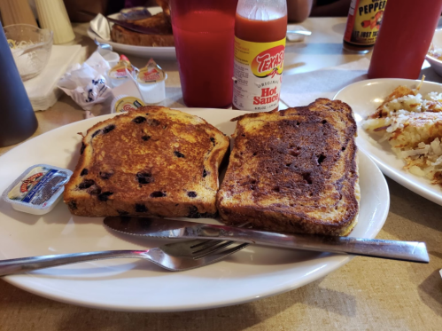 A plate with two slices of French toast, syrup, and hot sauce, alongside a side of rice.