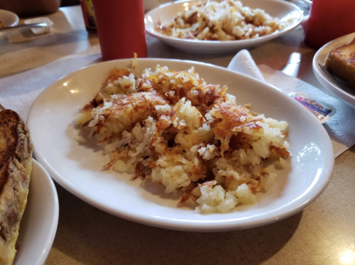 A plate of golden-brown hash browns served at a diner, with other dishes in the background.