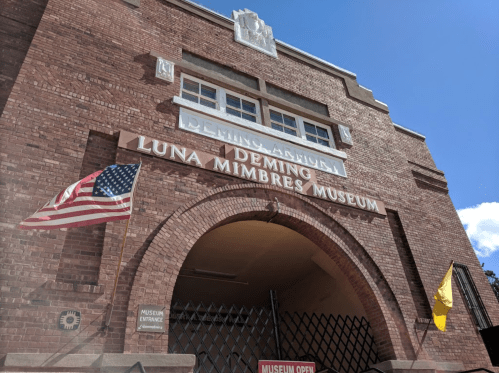Exterior of the Deming Luna Mimbres Museum, featuring brick architecture and flags, with a clear blue sky above.