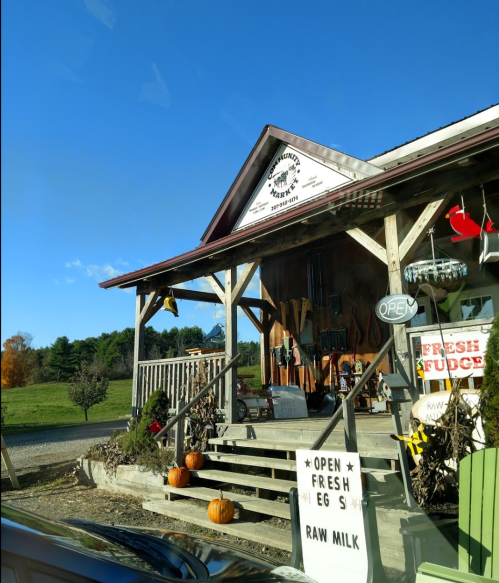 A rustic store with a wooden porch, signs for fresh eggs and raw milk, and autumn decorations like pumpkins.