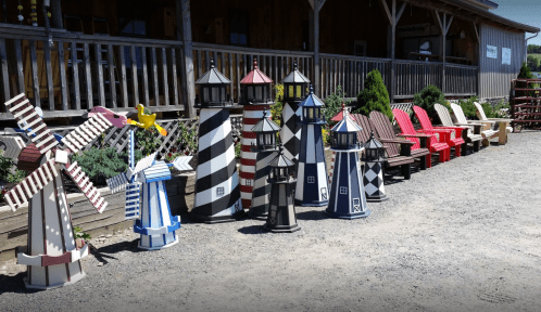 Colorful decorative lighthouses and chairs arranged outside a wooden building on a gravel path.