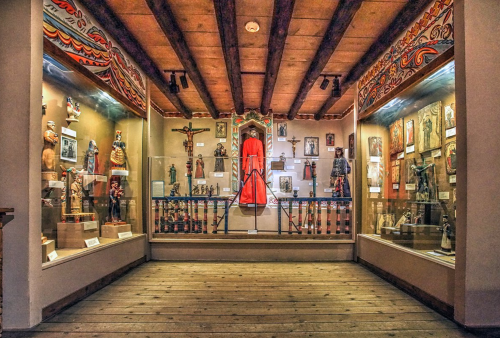 A museum display featuring various cultural artifacts, including statues and a red-draped figure, in a wooden room.