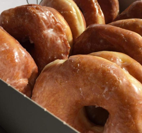 A close-up of glazed donuts stacked in a box, showcasing their shiny, golden-brown surface.