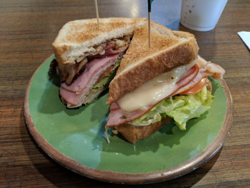 A toasted sandwich with layers of ham, turkey, cheese, and lettuce, served on a green plate.