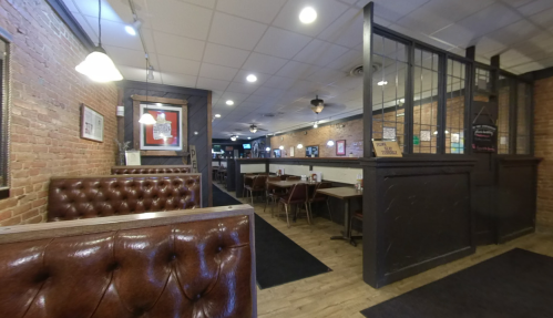 Interior of a cozy restaurant featuring brick walls, wooden floors, and booths with tufted leather seating.