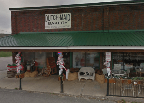 A quaint bakery storefront with a green awning, festive decorations, and a sign reading "Dutch-Maid Bakery."