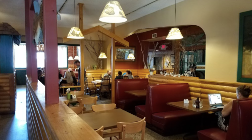 Cozy restaurant interior with wooden decor, booths, and diners enjoying meals in a warm, inviting atmosphere.