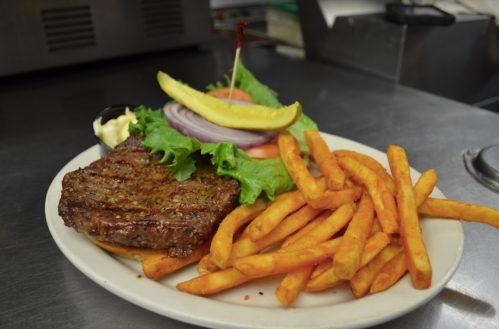 A juicy burger with lettuce, tomato, onion, and pickle, served with crispy fries on a white plate.