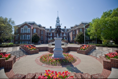 Statue of Liberty Independence surrounded by flowers and brick pathways in a sunny courtyard with buildings in the background.