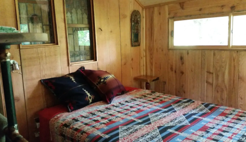 Cozy wooden bedroom featuring a patterned quilt, decorative pillows, and a window with natural light.
