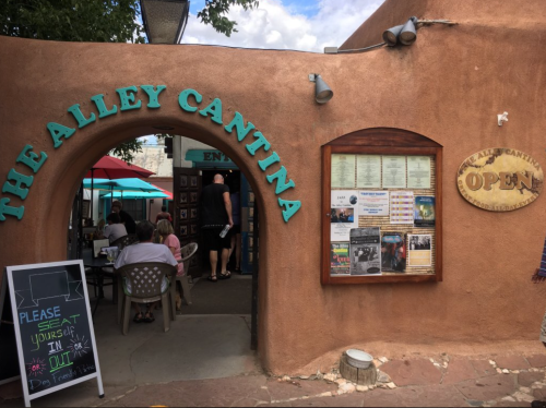 Entrance to The Alley Cantina with outdoor seating, a menu board, and a sign indicating it's open.