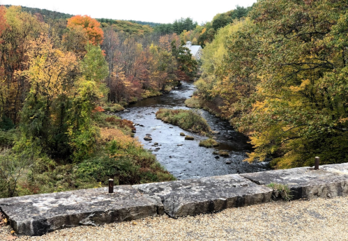 A serene river flows through a vibrant autumn landscape with colorful trees and a distant house.
