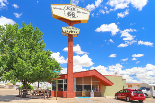 A retro diner with a large Route 66 sign, surrounded by trees and a blue sky with fluffy clouds.