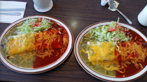 Two plates of enchiladas topped with cheese, served with lettuce and tomatoes on the side, one with red sauce and one with green.