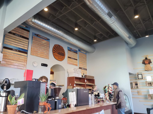 Interior of a café with a counter, menu boards on the wall, and customers ordering drinks. Bright and inviting atmosphere.
