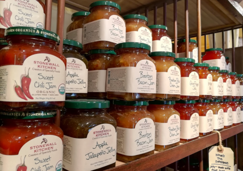 A shelf filled with various jars of jams and jellies, including sweet chili jam and bacon jam, from Stonewall Kitchen.