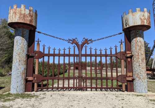 Rusty castle-style gate with towers, chains, and pointed spikes, set against a clear blue sky.