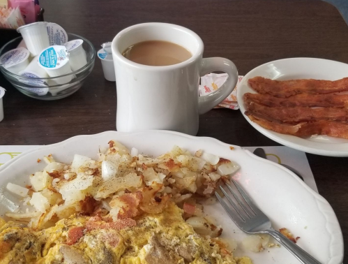 A plate of breakfast with an omelet, hash browns, a side of bacon, and a cup of coffee on a table.