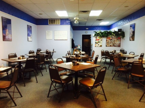A spacious, empty dining room with tables and chairs arranged, featuring blue walls and a ceiling fan.