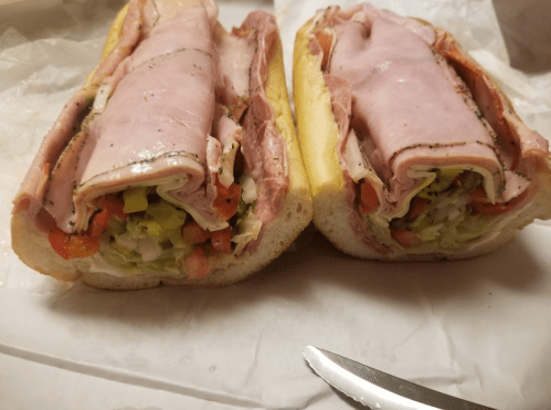A freshly cut sub sandwich filled with layers of ham, lettuce, tomatoes, and other toppings on a soft hoagie roll.