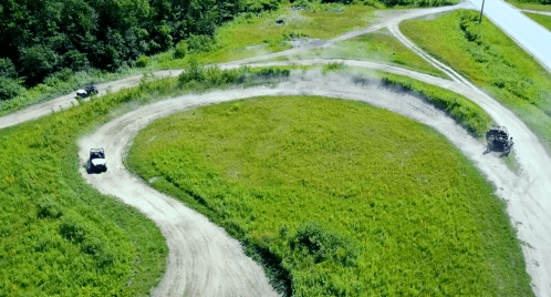 Aerial view of a dirt track winding through green fields, with a vehicle drifting on a curve.