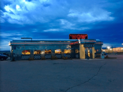 A retro diner named "WOW" with neon lights, set against a dramatic blue sky at dusk.