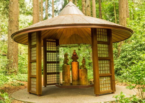 A wooden pavilion surrounded by trees, featuring glass displays of sculptures inside.