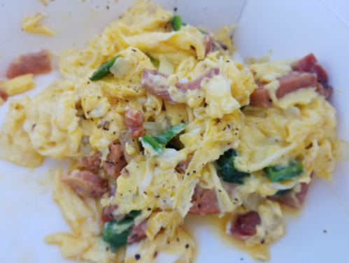 Scrambled eggs mixed with diced ham and green peppers, served in a white container.